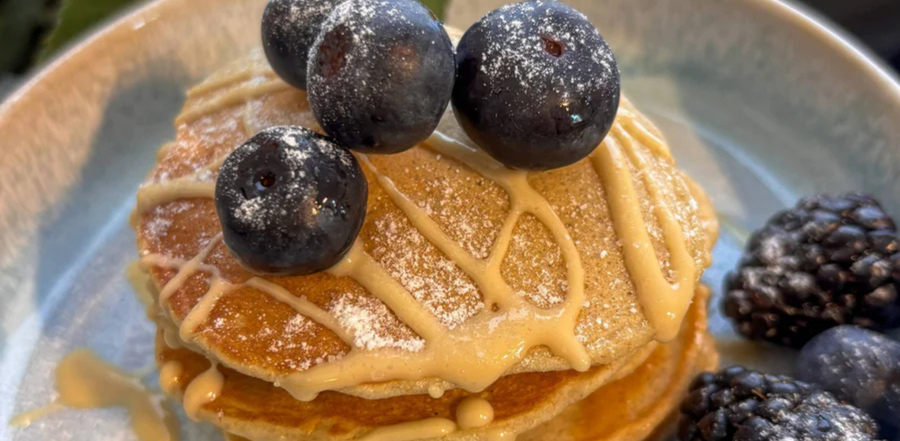 A well-crafted alt teClose-up of a stack of gluten-free banana pancakes drizzled with almond butter and dusted with sugar, garnished with blueberries and raspberries