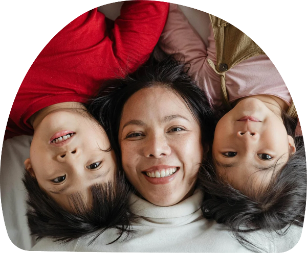 Asian mother lying on her back with two children, close-up on their faces, expressing warmth and connection